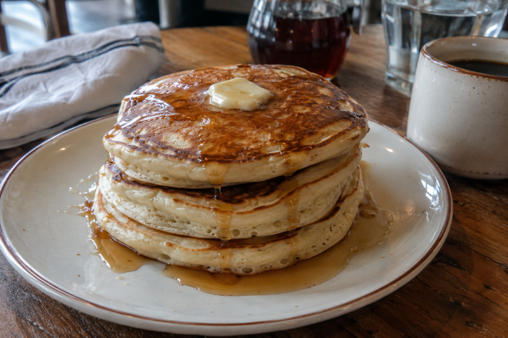 Stack of fluffy homemade pancakes with butter and maple syrup served on a rustic breakfast table.